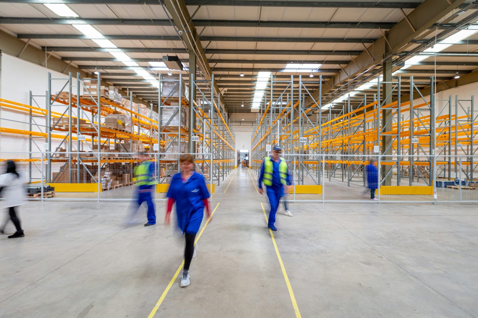 Modern distribution warehouse with staff moving inventory between pallet racks